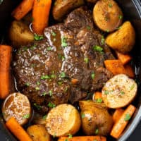 A Crock Pot Roast in a Slow Cooker with potatoes and carrots with gravy.