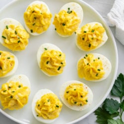 Deviled Eggs on a white plate topped with chives and paprika.