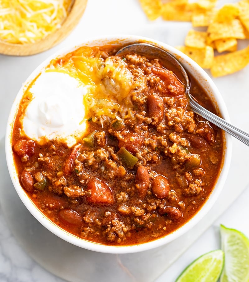 A white bowl of Chili with sour cream and cheese on top.