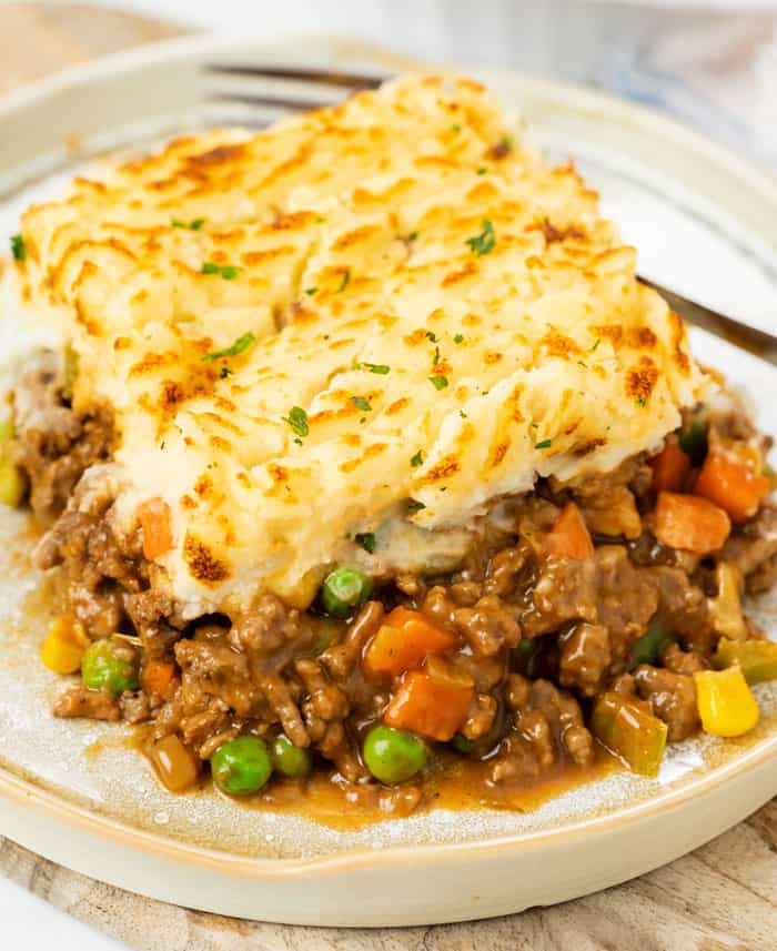A plate with a slice of easy shepherds pie with ground beef with a fork in the background.