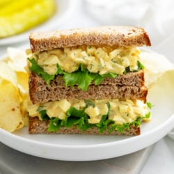 Two slices of Egg Salad Sandwiches stacked on top of each other with chips in the back.