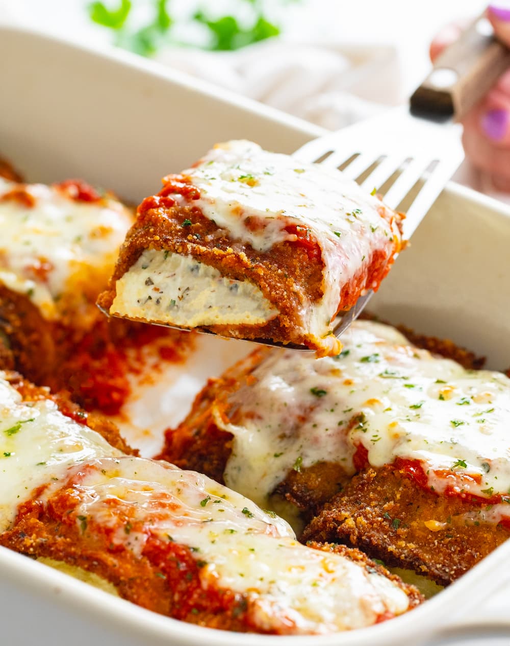 Eggplant Rollatini being pulled up from a casserole dish with a spatula.