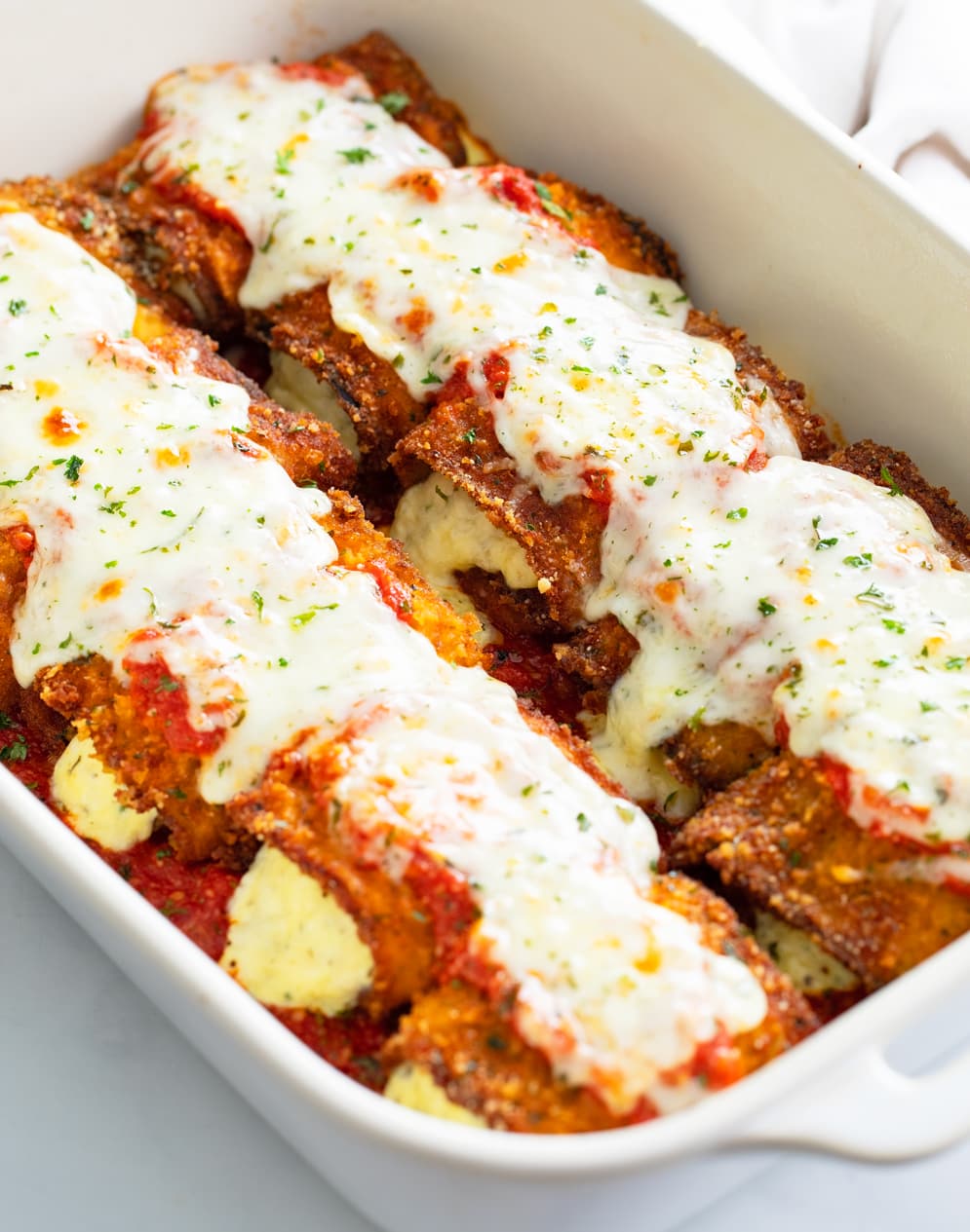 Side view of Eggplant Rollatini in a casserole dish topped with marinara sauce and mozzarella cheese.