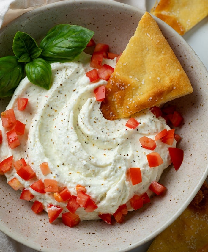 Feta Dip in a bowl topped with diced tomatoes, fresh basil, and a toasted Naan bread.