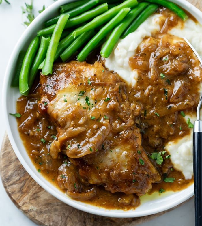 A plate with French Onion Chicken with mashed potatoes and green beans.