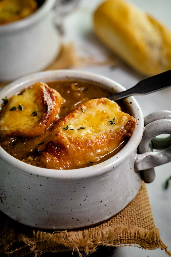 Two slices of baguette with melted cheese in a bowl of french onion soup and thyme on top. 