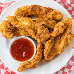 A white plate with fried chicken tenders with sweet and sour sauce.