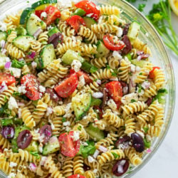 A glass bowl filled with Greek Pasta Salad.