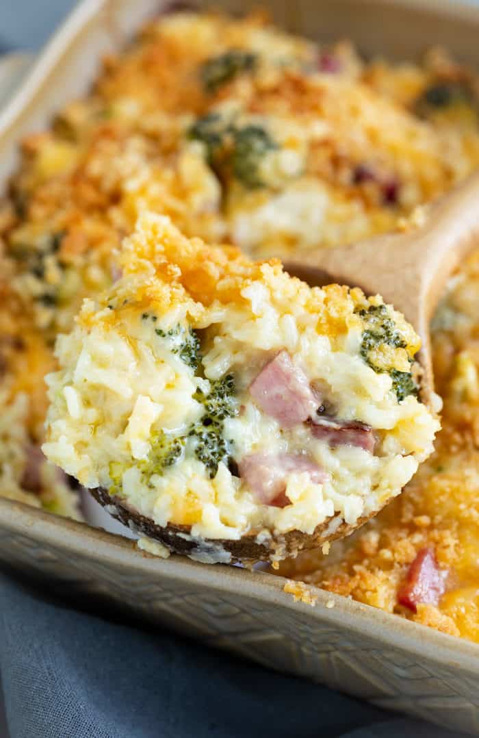 A wooden spoon full of ham casserole with broccoli and rice.