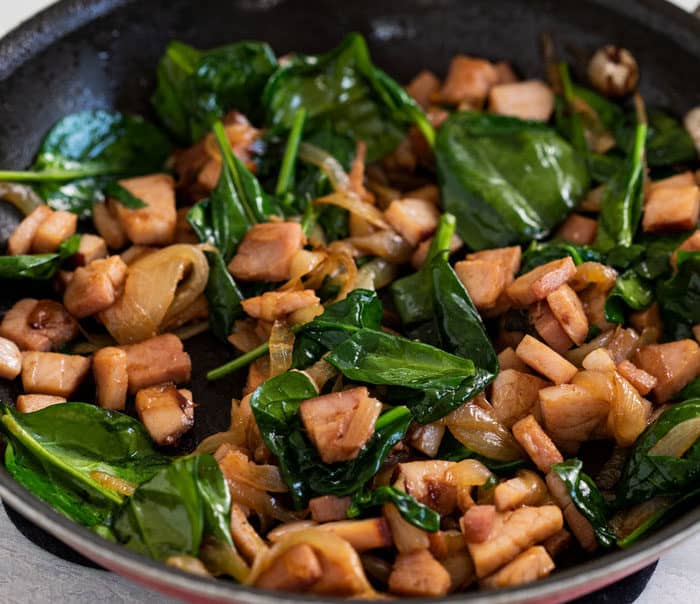 diced ham in a pan with caramelized onions and spinach.