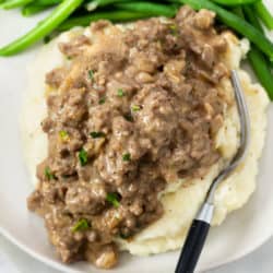 Hamburger Gravy over mashed potatoes with green beans in the background.