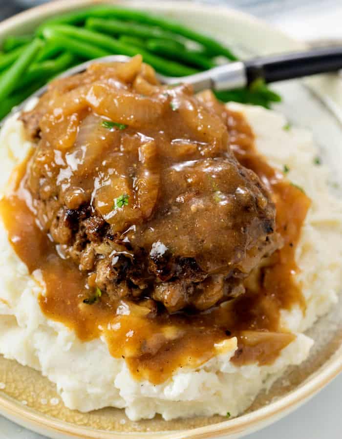 Hamburger Steak with Brown Gravy and Onions on a pile of mashed potatoes.