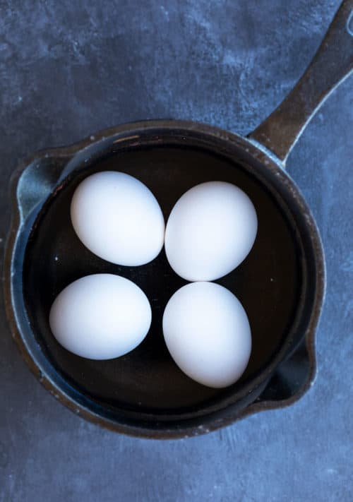 Overhead view of a cast iron pot filled with water and 4 hard boiled eggs on a dark blue surface.