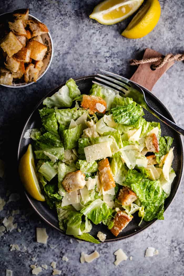 A plate with chicken caesar salad topped with croutons and Parmesan cheese.