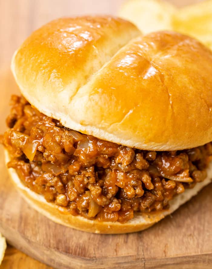 A burger bun filled with homemade sloppy joes on a wooden surface.