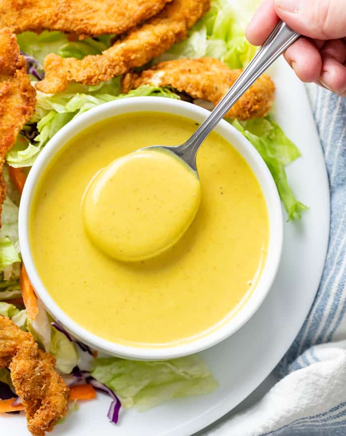 Overhead view of a white bowl of honey mustard with a spoon in it.