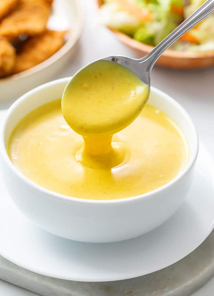 Honey Mustard in a white bowl with a spoon pouring it out.