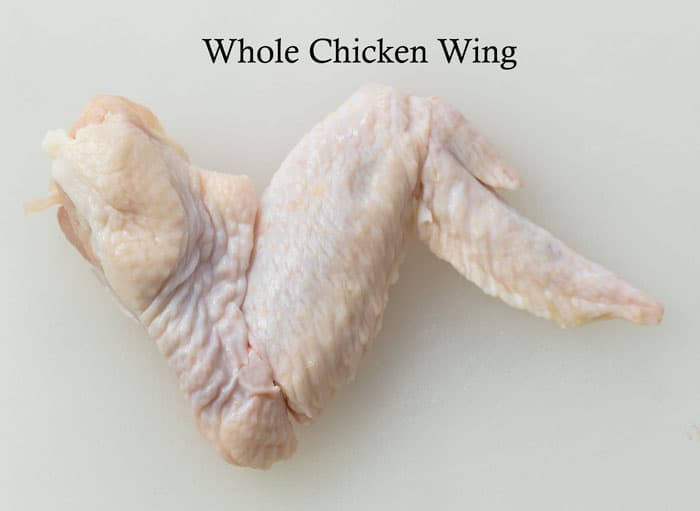 A whole chicken wing on a white surface before being separated into party wings.