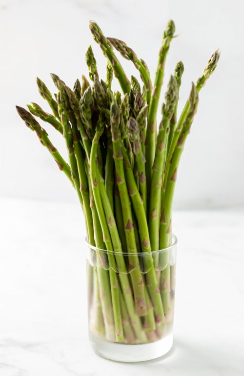 A glass of water with asparagus in it to keep it fresh. 
