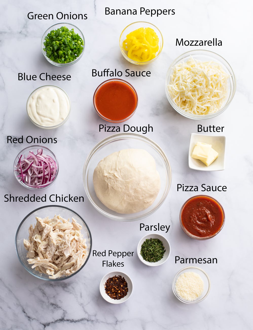 Ingredients for making Buffalo Chicken Pizza on a white surface.