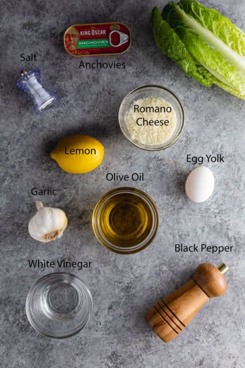 Ingredients needed to make homemade caesar dressing on a blue table.