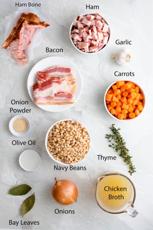 Birds eye view of ingredients on a white surface for making ham and bean soup.