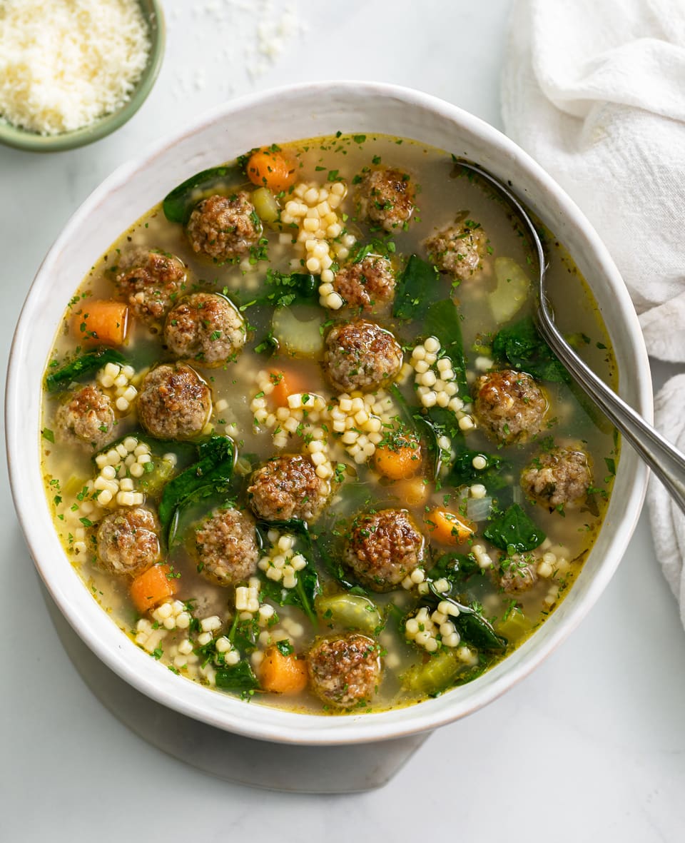 Italian Wedding Soup in a white bowl with meatballs, spinach, and acini de pepe.