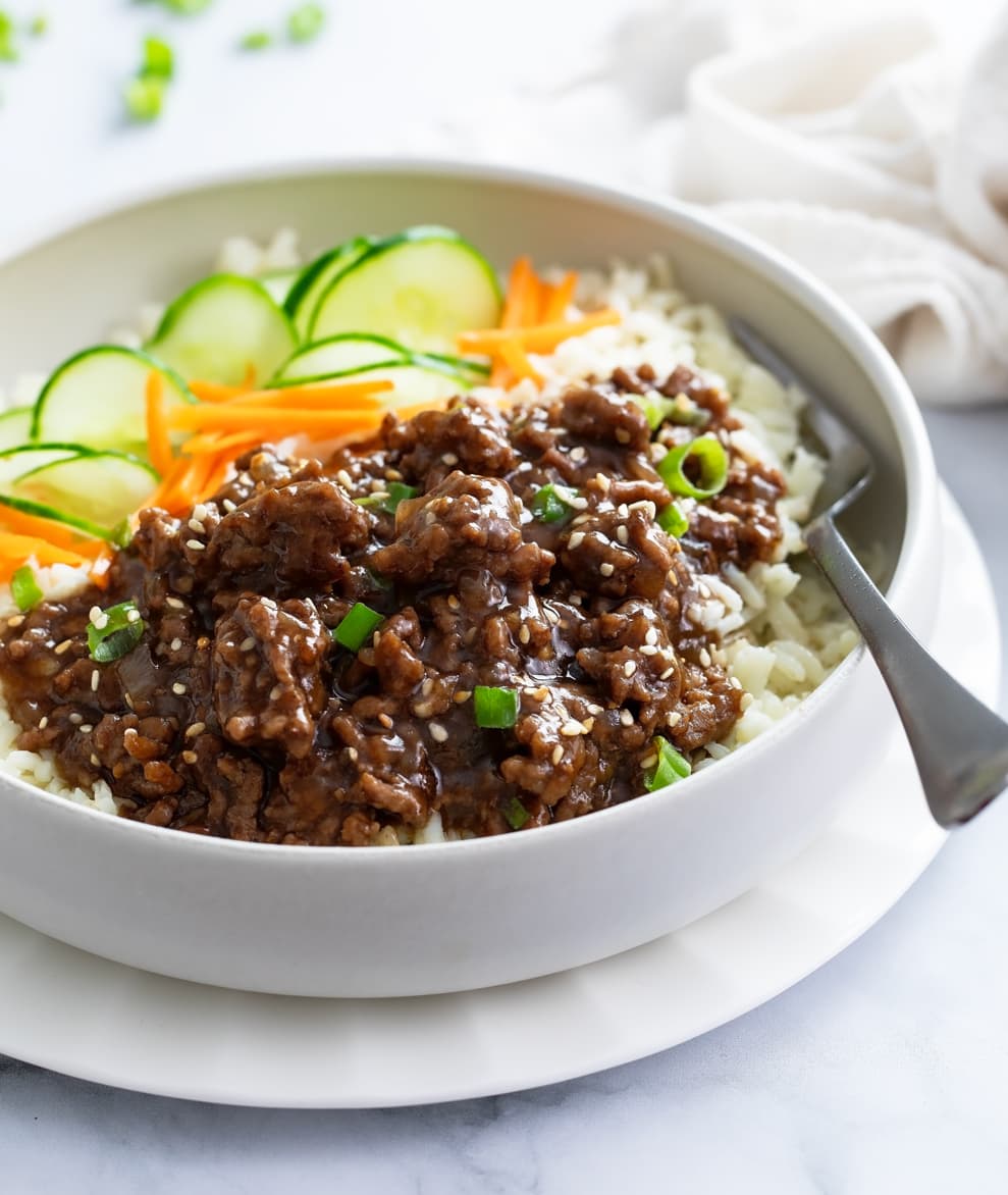 Korean Beef Bowls filled with rice, ground beef in sauce, cucumbers, and carrots.