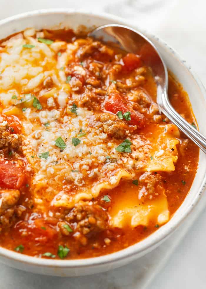 A white bowl filled with Lasagna Soup topped with cheese with a spoon in the back.