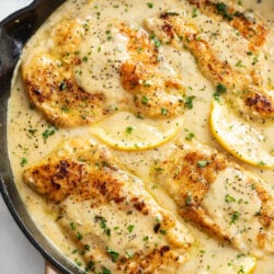 Lemon Pepper Chicken in a skillet with lemon wedges and sauce.