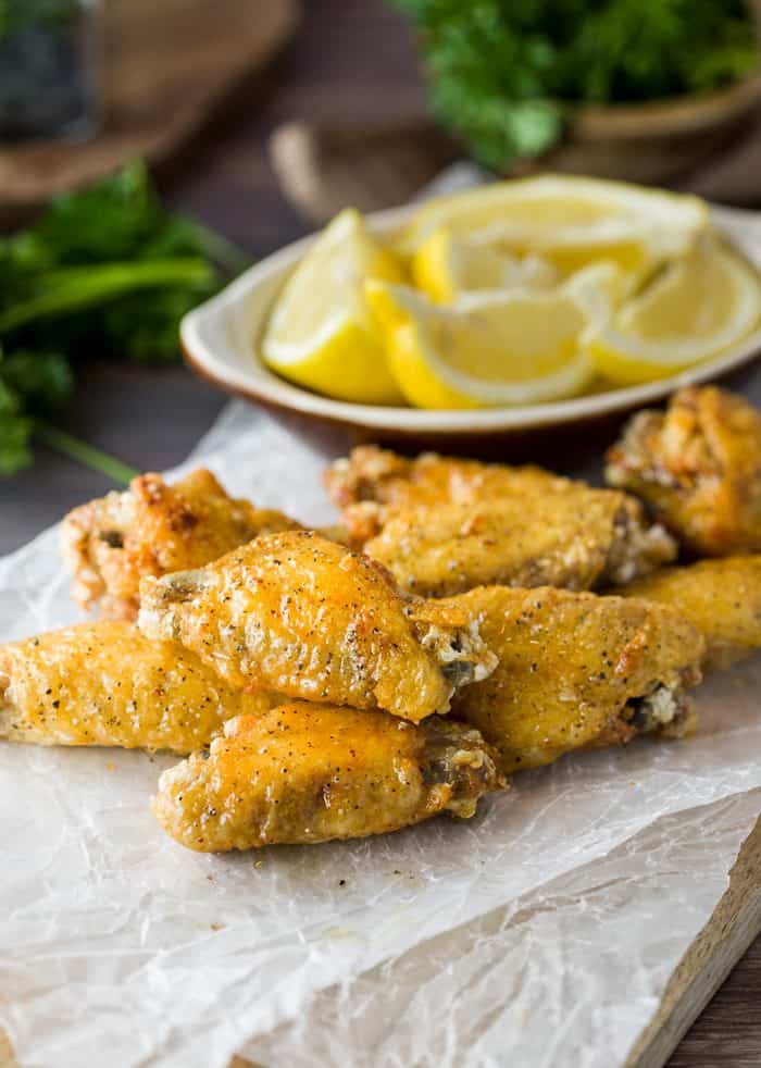 Lemon Pepper Wings on a piece of white wax paper which a bowl of sliced lemons in the background.