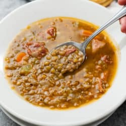 A white bowl full of lentil soup with ham and spoon scooping it up.