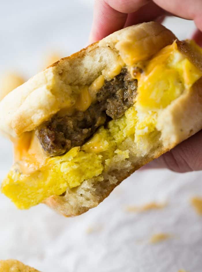 A close up view of a hand holding a sausage egg and cheese sandwich with a bite taken out of it.