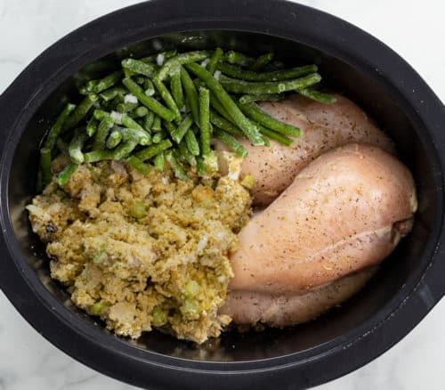 Uncooked stuffing, green beans, and chicken breasts in a crock pot.