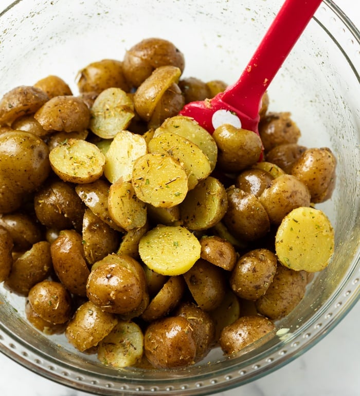 A glass bowl with potatoes tossed in seasoning and oil before being roasted.
