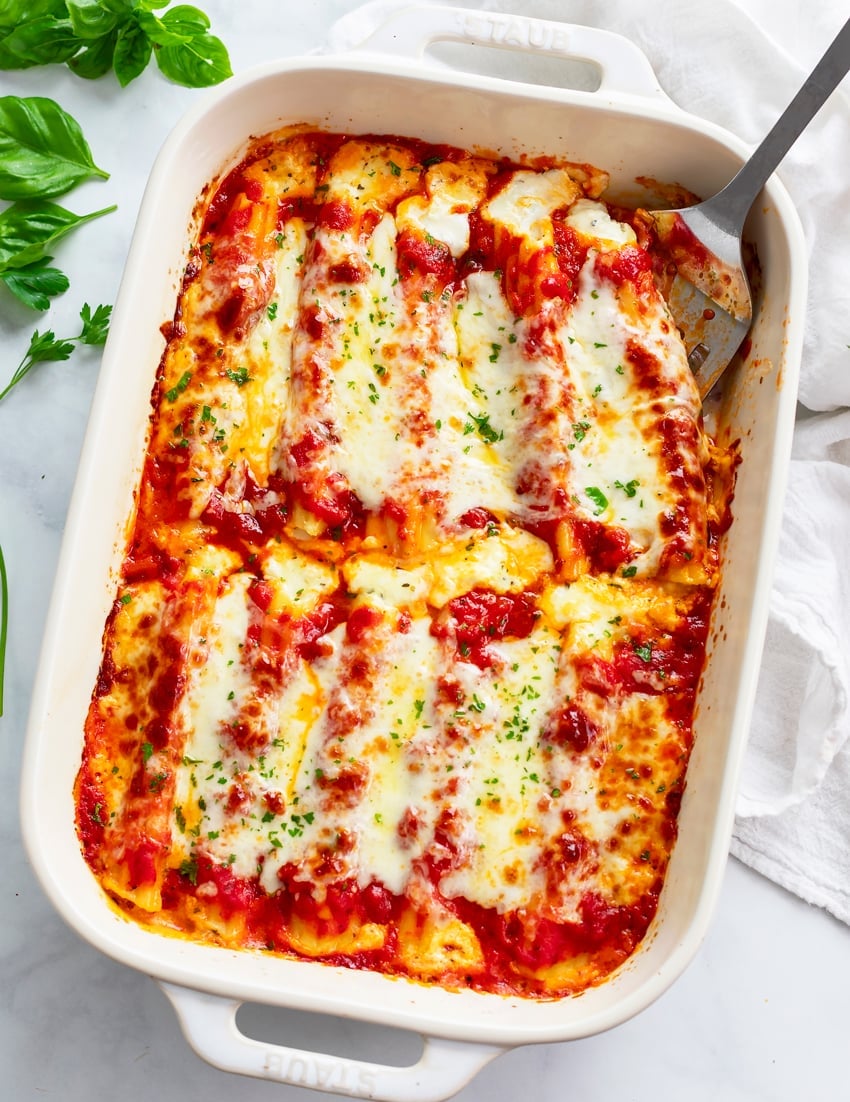 Cheese filled manicotti in a white casserole dish with a spatula on the side.