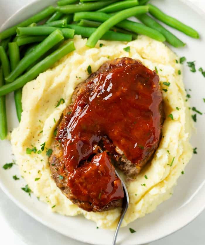 Mini Meatloaf topped with glaze on a pile of mashed potatoes with green beans.