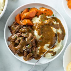 Mississippi Pot Roast on a white plate with carrots, mashed potatoes, and gravy.