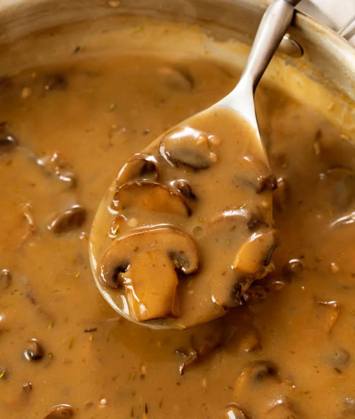 A spoon full of thick and creamy mushroom gravy from a skillet.