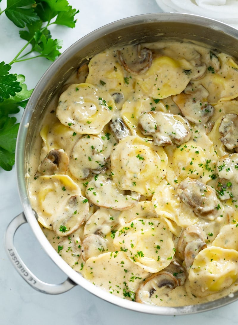 A skillet filled with ravioli in a creamy mushroom sauce with fresh parsley on top.