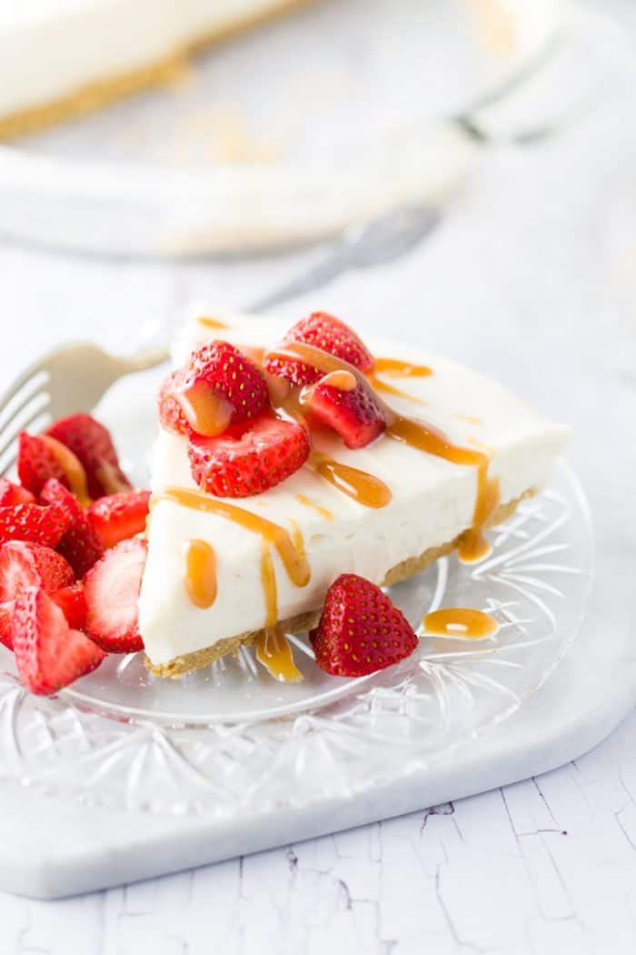 White cheesecake with caramel drizzled on top with fresh strawberries on a glass plate.