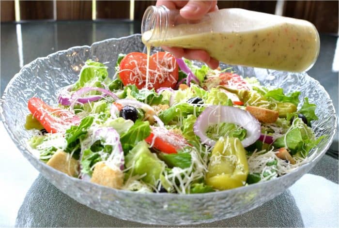 copycat olive garden salad dressing being poured over a large glass bowl filled with olive garden salad.