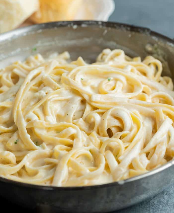 Creamy Fettuccine Alfredo in a skillet with rolls in the background.