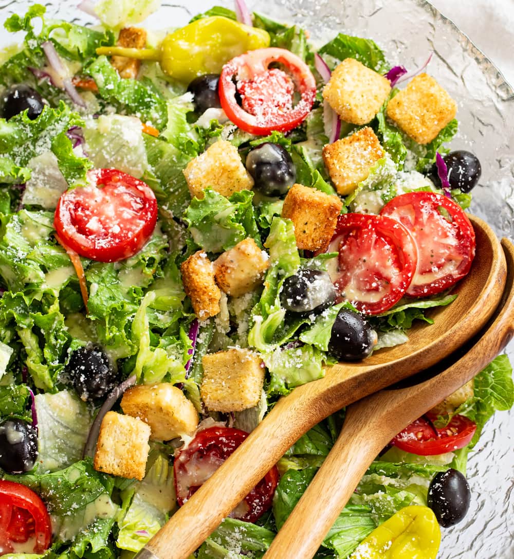 Olive Garden Salad in a glass bowl with wooden kitchen tongs.