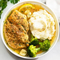 Pan Fried Chicken with pan sauce on a white plate with mashed potatoes and broccoli.