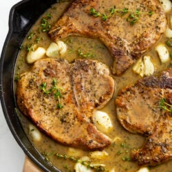 Pan Fried Pork Chops in a skillet with a pan sauce, garlic, and thyme.