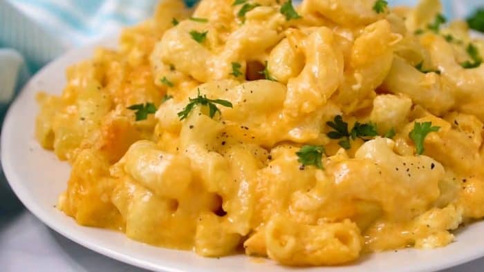Creamy macaroni and cheese on a white plate topped with chopped parsley.