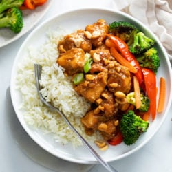A white plate with rice and peanut butter chicken with stir-fried vegetables.