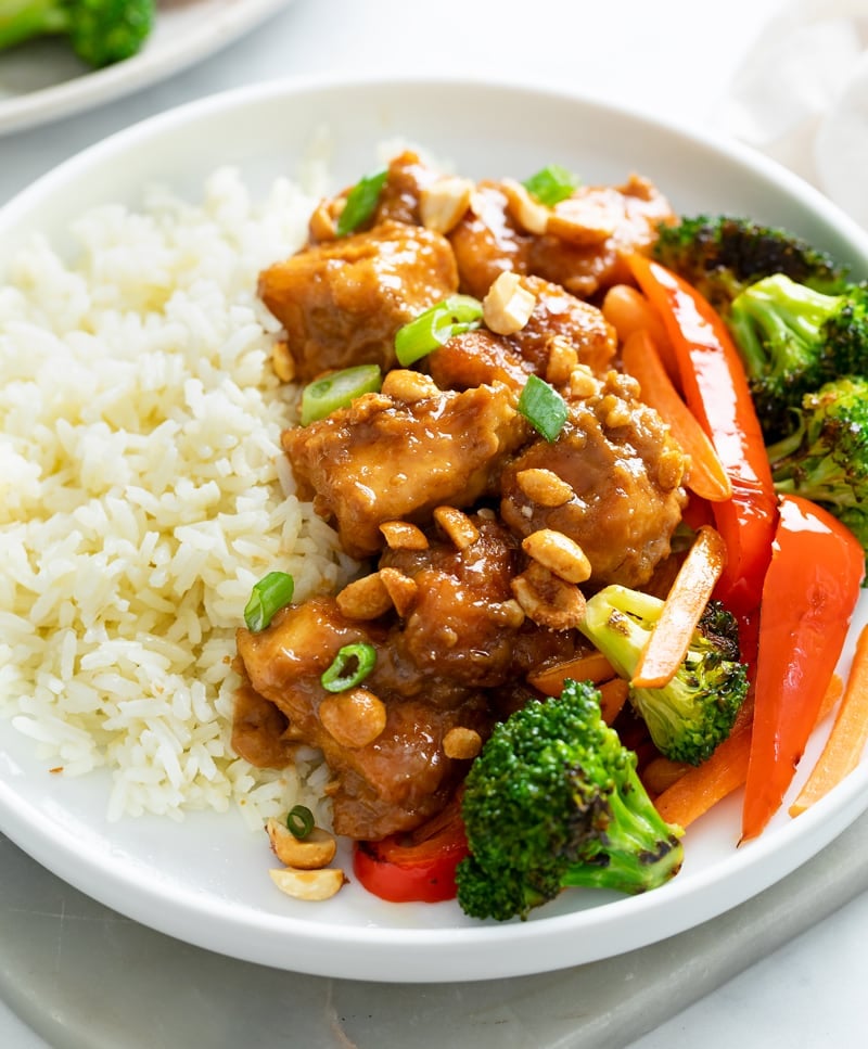 A white plate with Peanut Butter Chicken, rice, and vegetables.