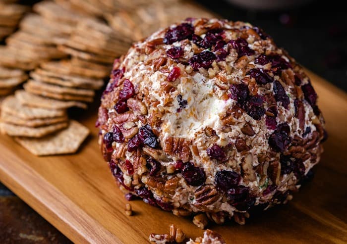 A pineapple pecan cheese ball on a wooden cutting board with crackers in the background.